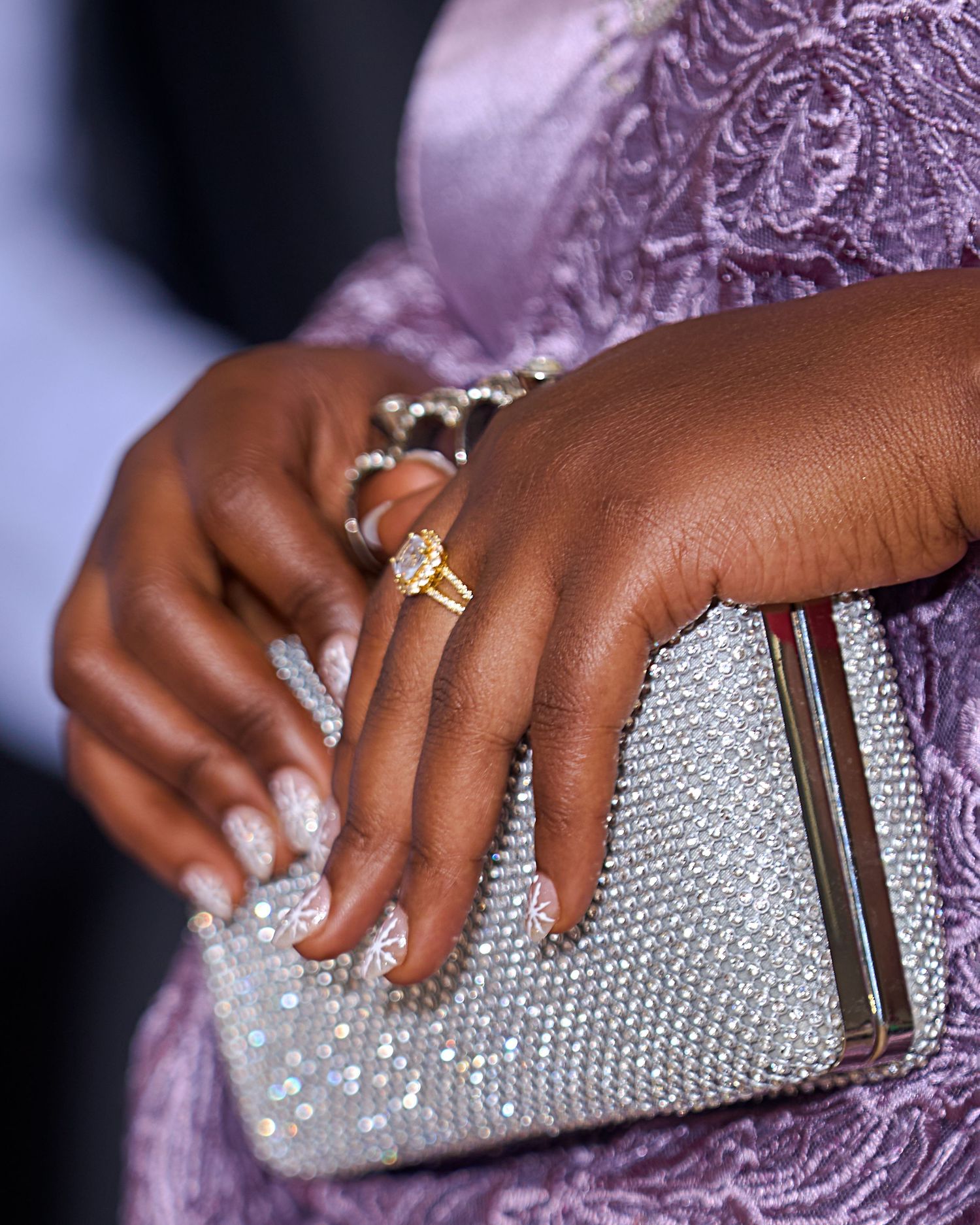Close-up of sparkling crystal clutch purse with rings on hand.