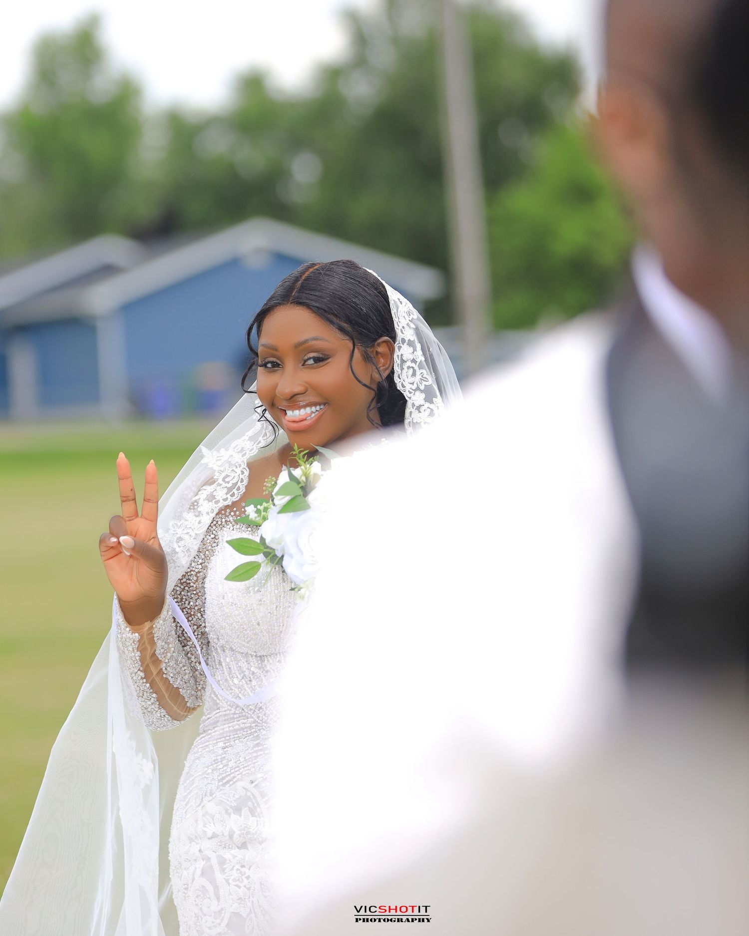 Bride in white lace gown and veil poses outdoors during wedding photoshoot.