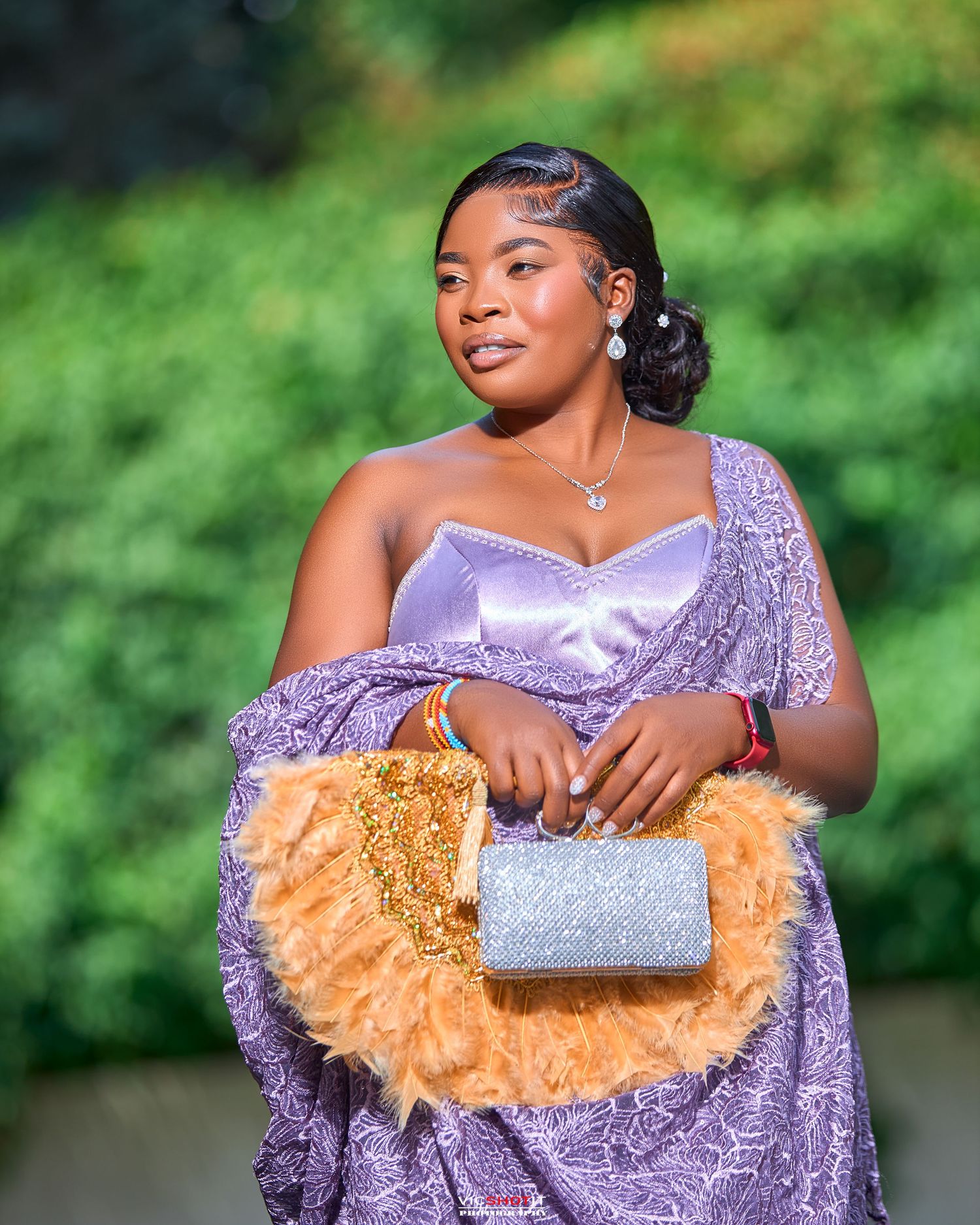 Woman in purple gown with gold details holding a silver clutch purse.