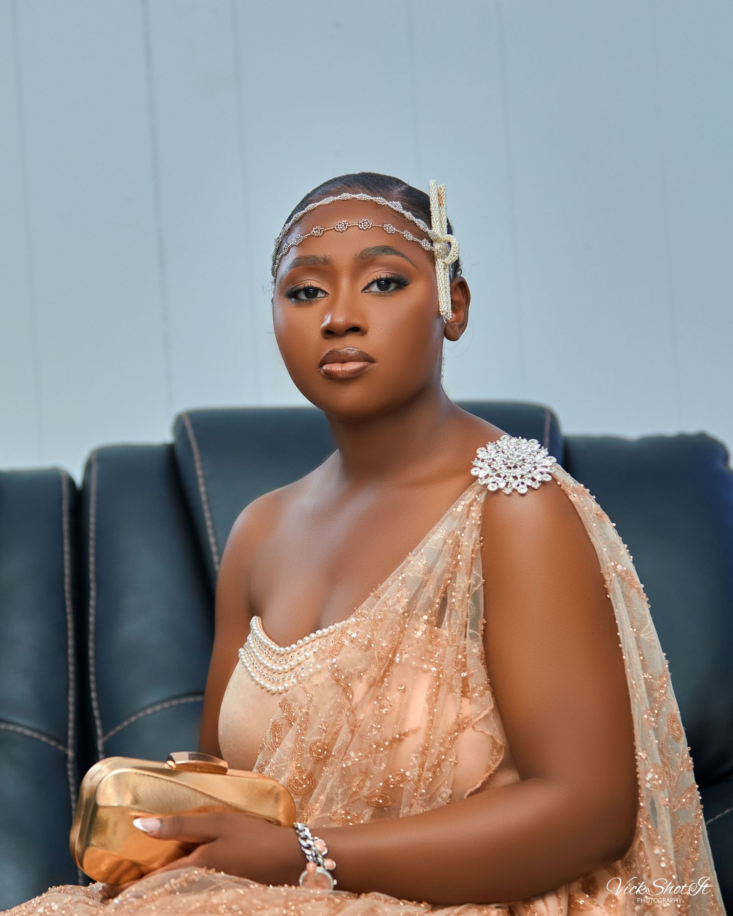 A woman in a peach-colored beaded dress poses on a dark couch.