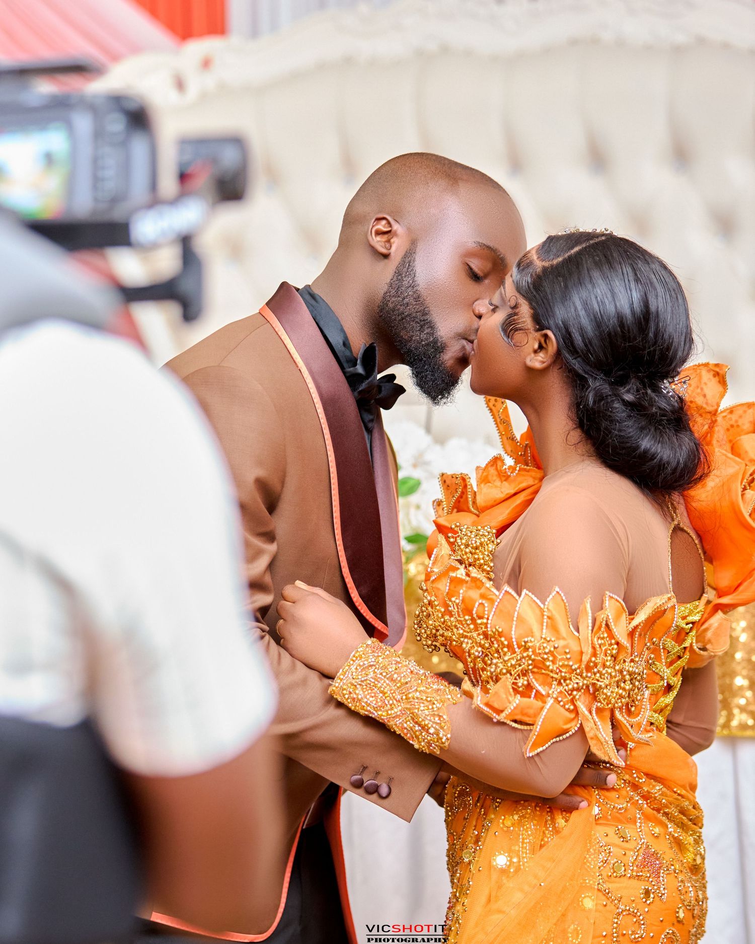 Romantic couple in formal attire sharing intimate moments in an orange-themed photoshoot.