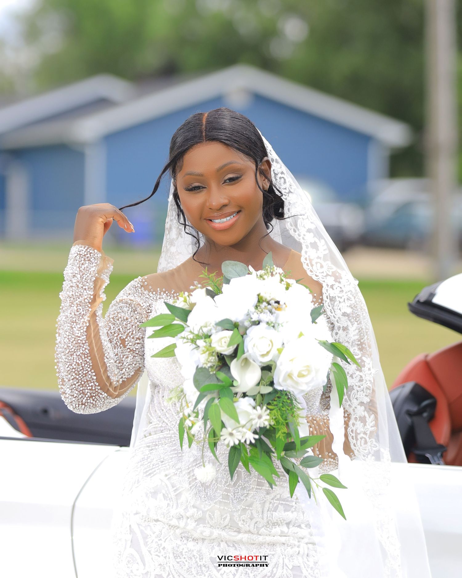 Bride in sparkling white gown holding bouquet of white lilies during outdoor photoshoot.