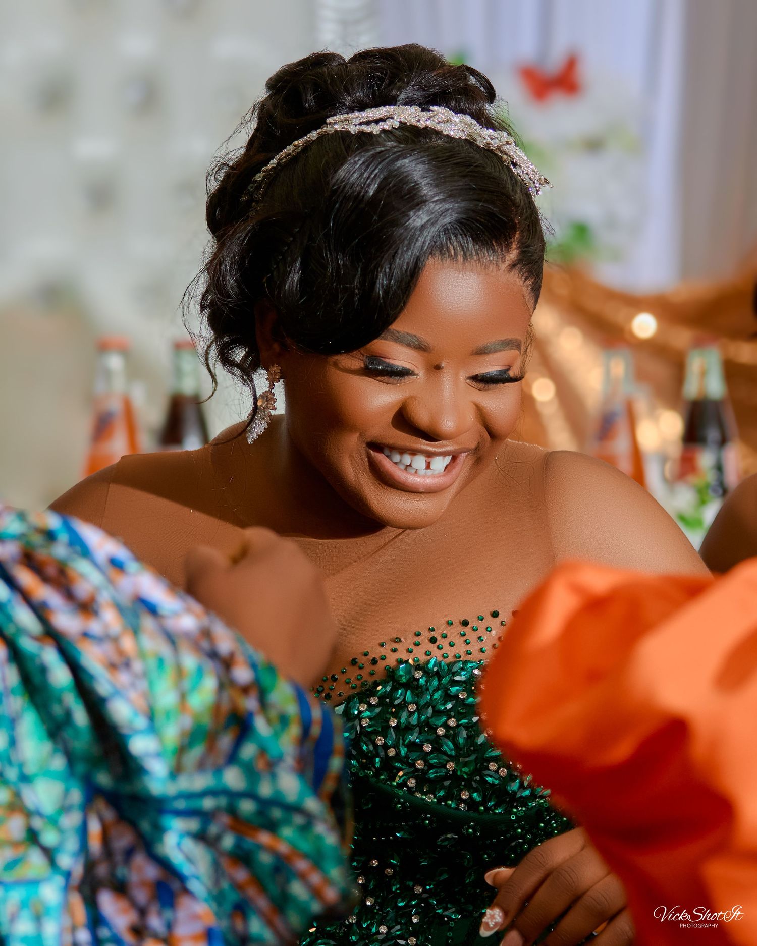 A woman wearing a sparkling emerald green gown smiles brightly at a celebration.