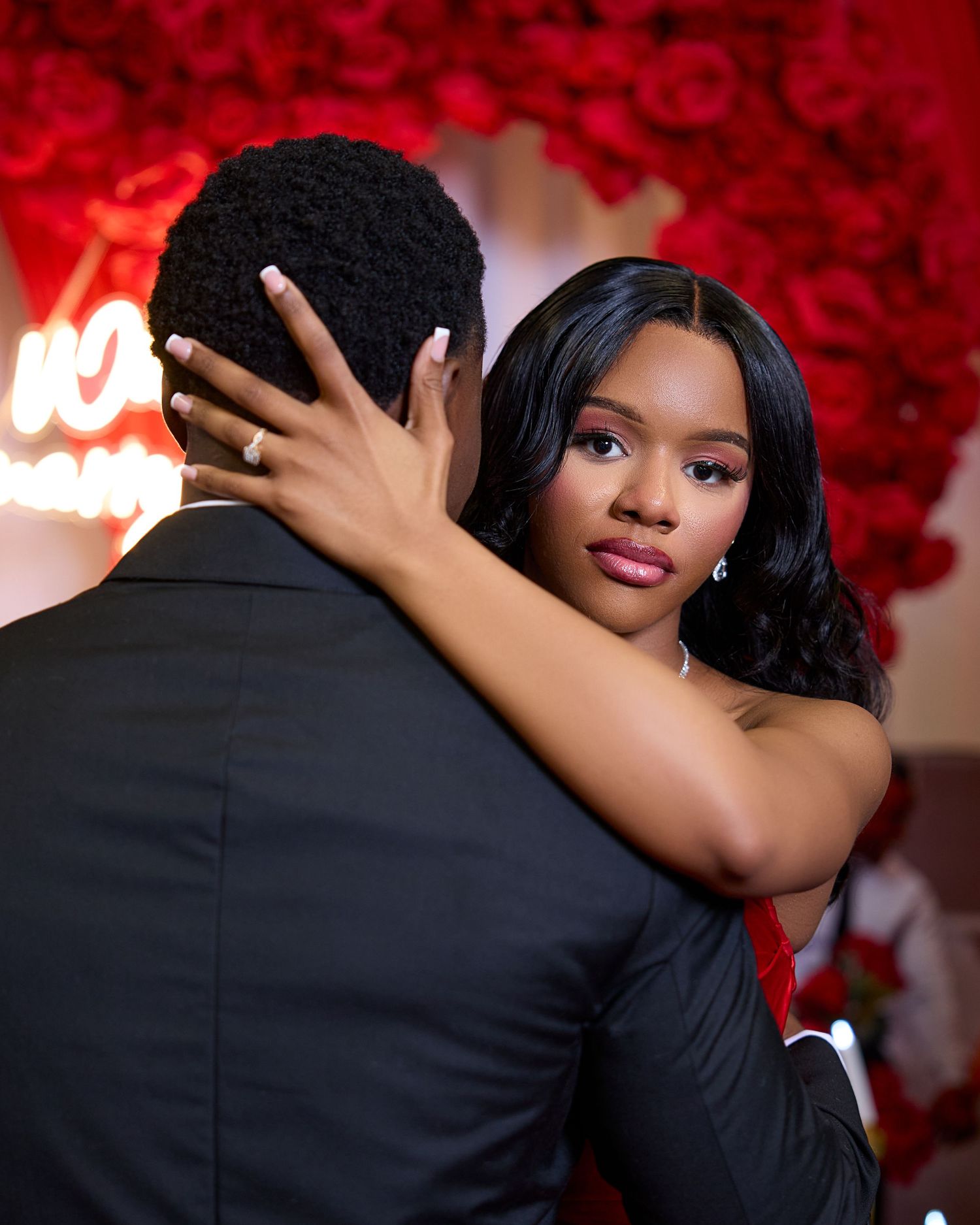 A romantic couple embraces while dancing against a backdrop of red roses at an elegant event.