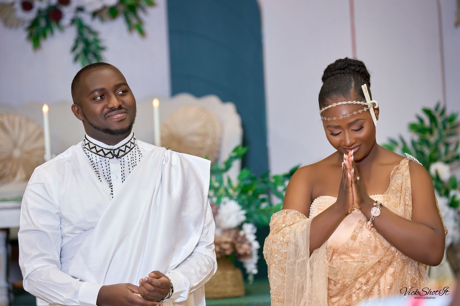 A couple in white and champagne colored formal attire shares a moment during a ceremony.
