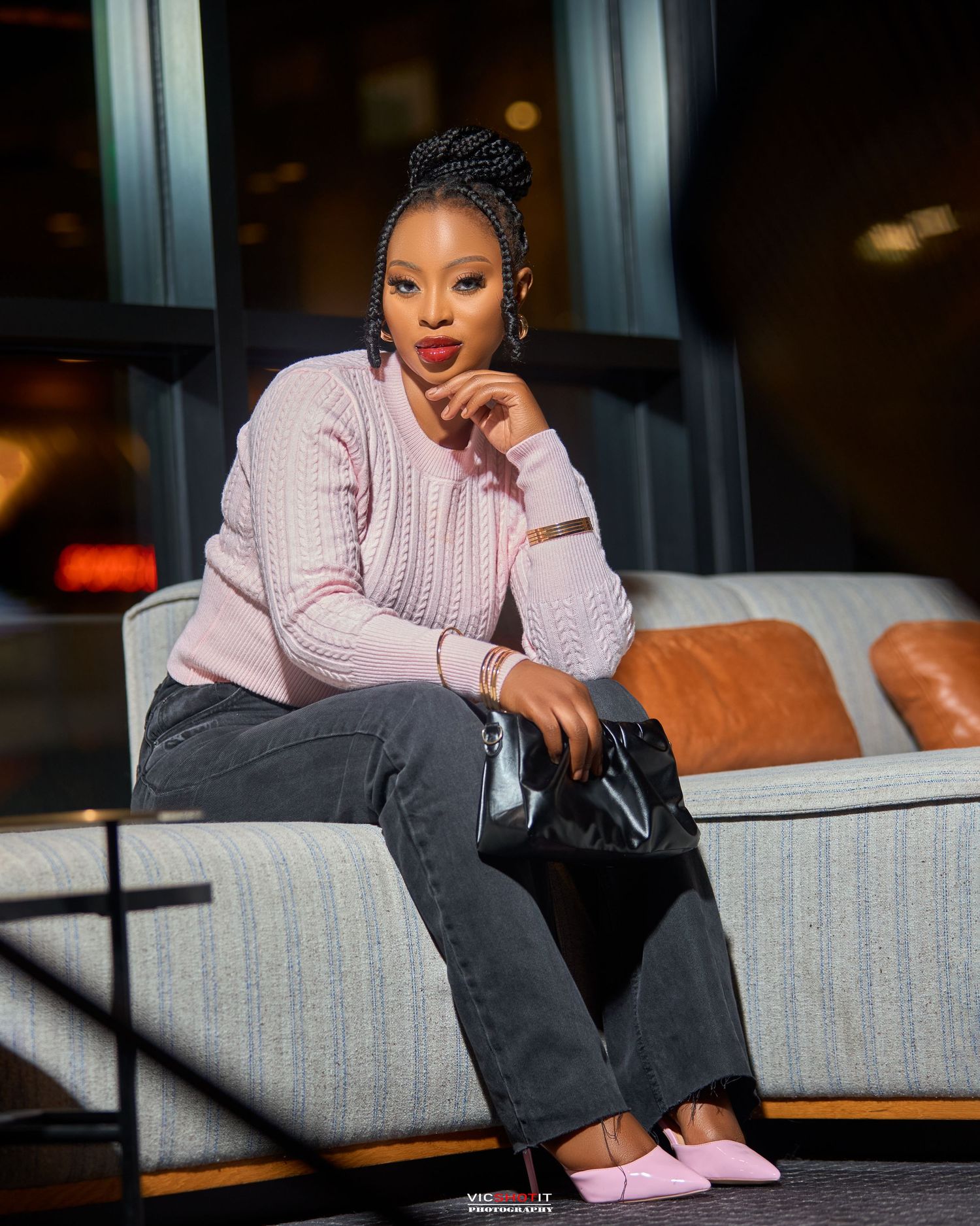 Casual portrait session on striped couch featuring pink sweater and dark denim outfit.