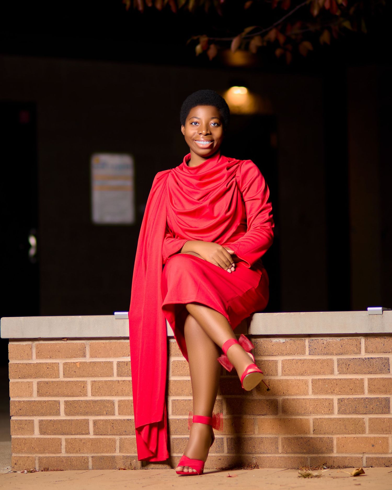 Model in a flowing red ensemble poses elegantly on a brick wall during an evening photoshoot.