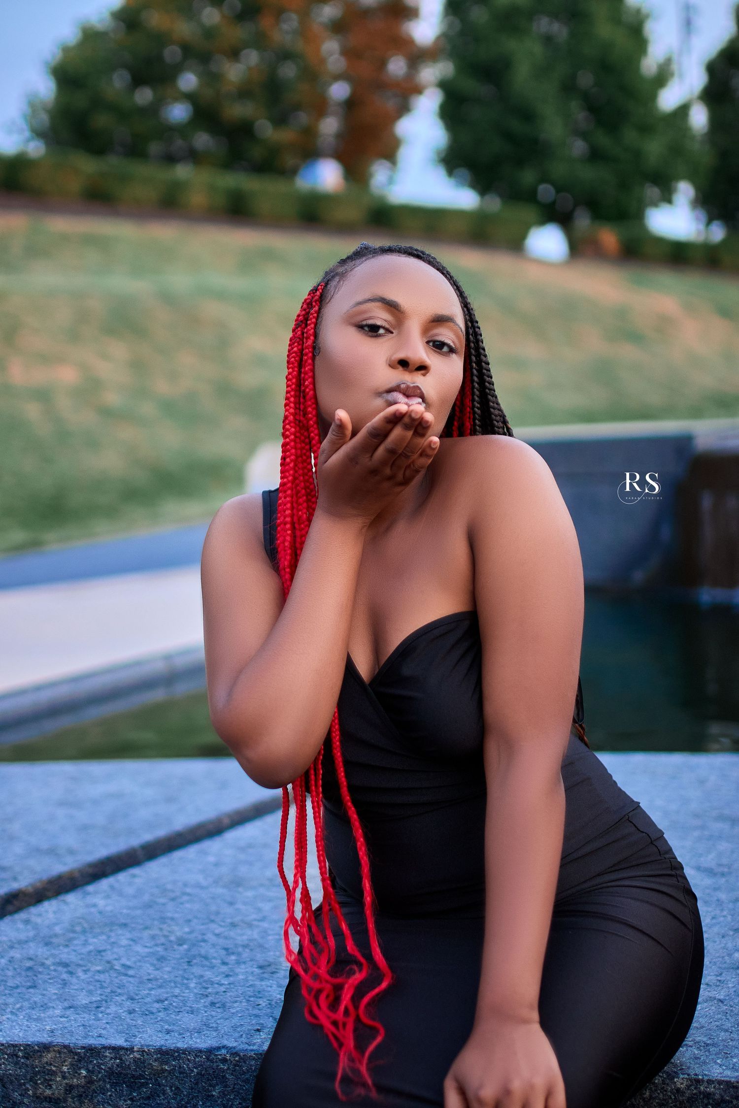 Artistic outdoor photoshoot featuring someone in black attire with striking red braids against a natural background.