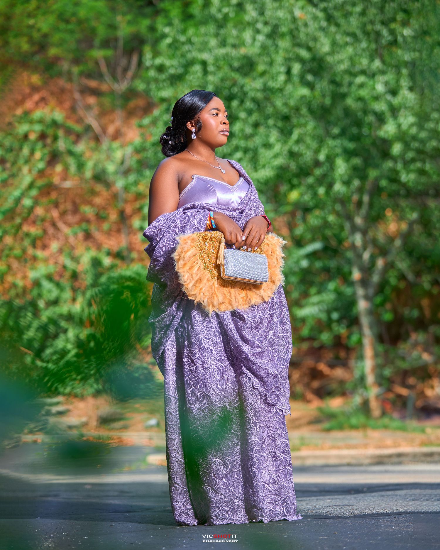Woman in lavender dress with peach accents poses elegantly outdoors.