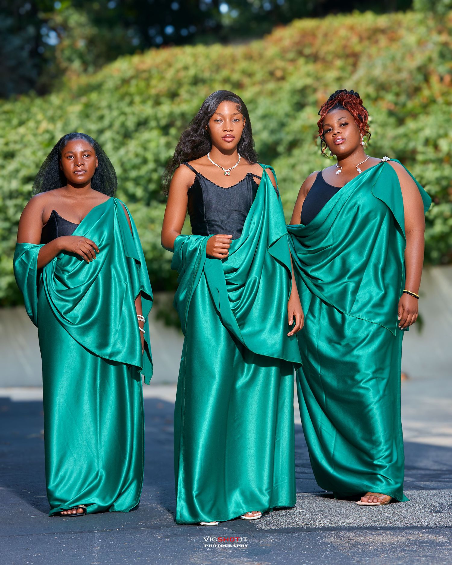 Group photo of people in emerald green formal dresses posing together outdoors.