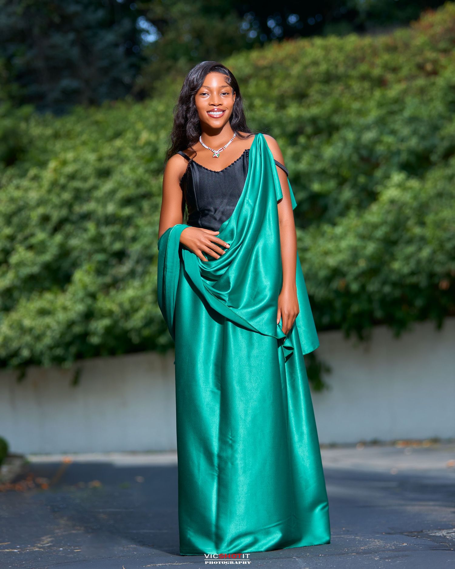 Group wearing flowing emerald green dresses pose dramatically on pavement.