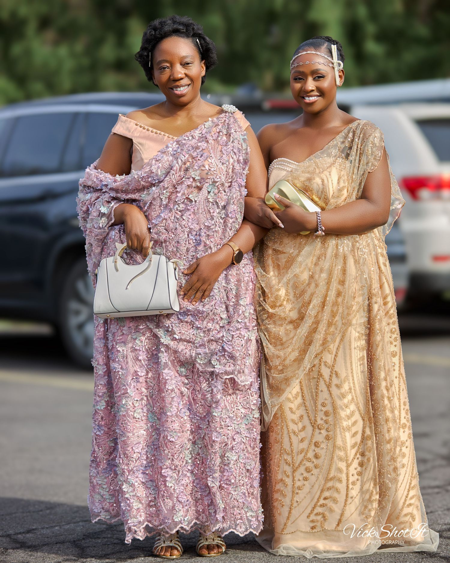 Two friends in flowing evening gowns pose together in a parking lot.