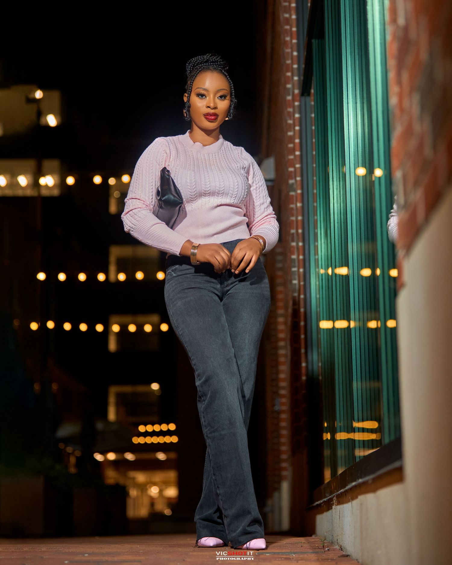 Person in pink sweater and jeans relaxes on modern couch in atmospheric evening setting.