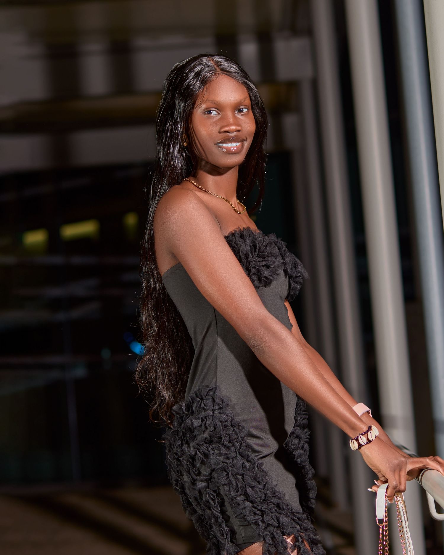 Evening fashion portrait of a model in a textured black dress against modern architecture.