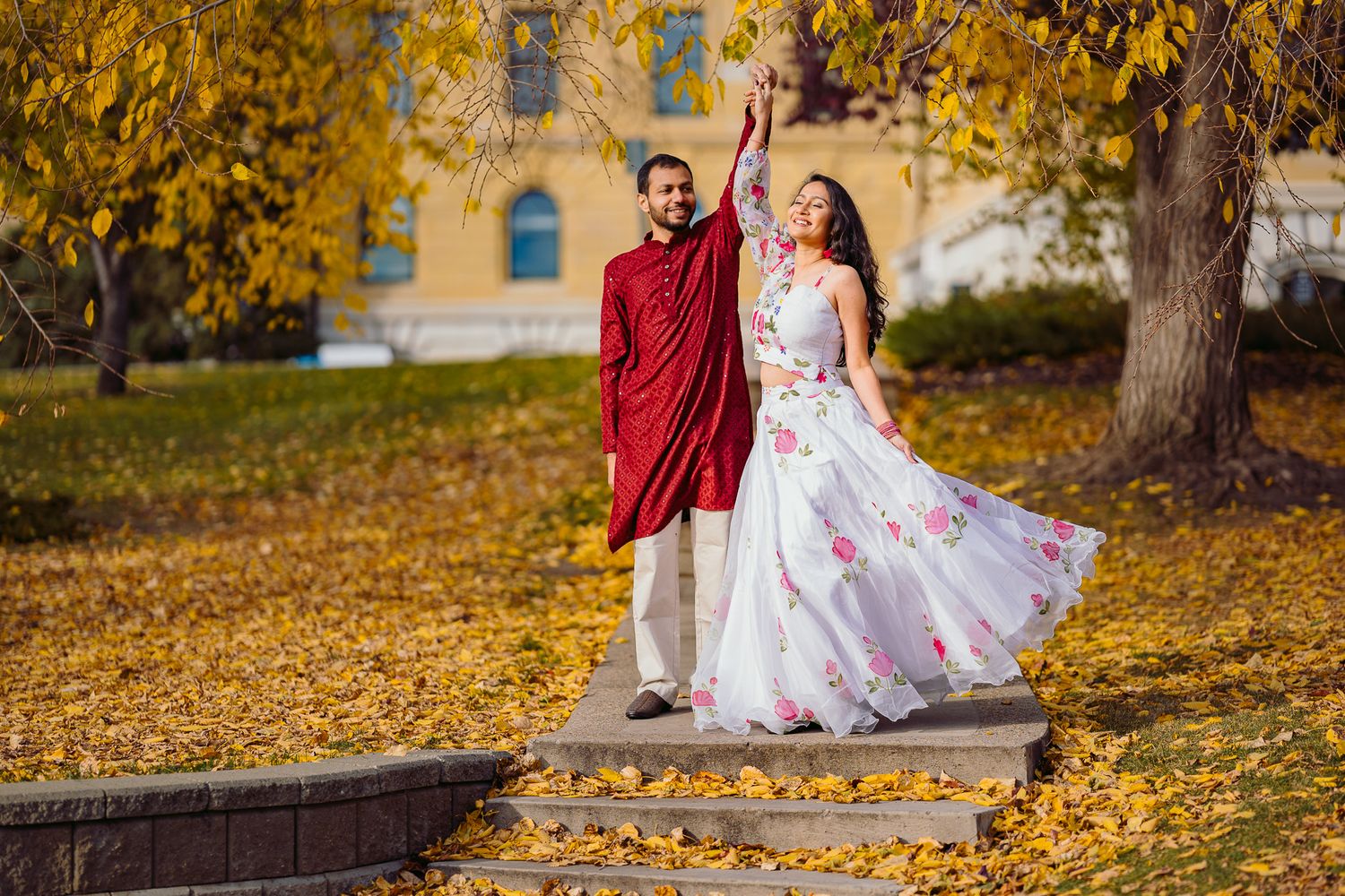 Indian Groom twirling Indian bride in beautiful traditional clothes with Edmonton legislature building as backdrop