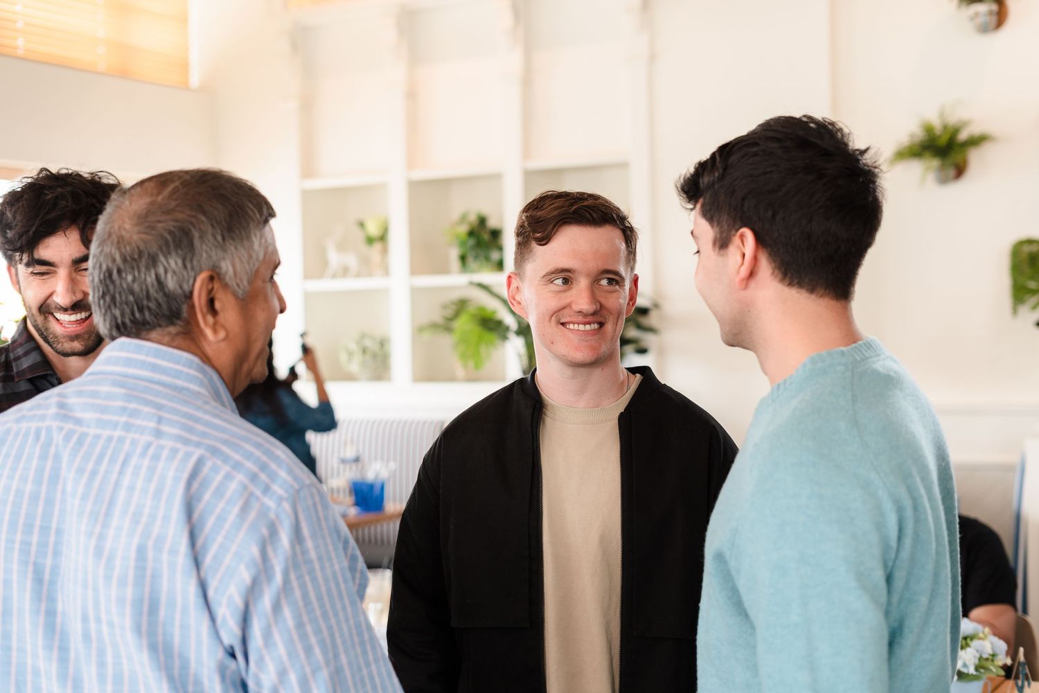 Small group having a friendly conversation while standing in a bright modern office space with white built-in shelves.