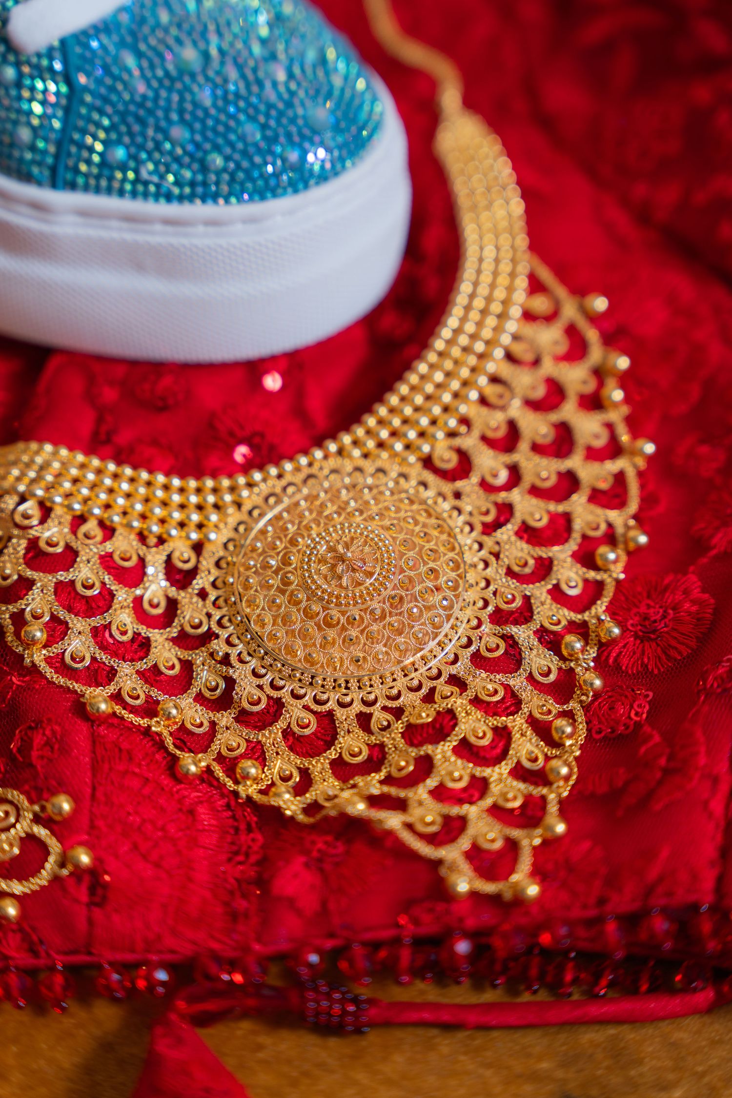 Ornate gold bridal necklace with intricate design patterns displayed on red velvet fabric.