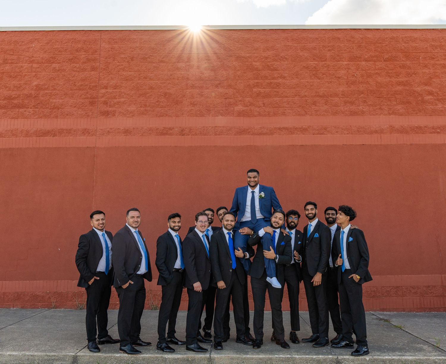 Creative groomsmen photo with one standing elevated against red wall.