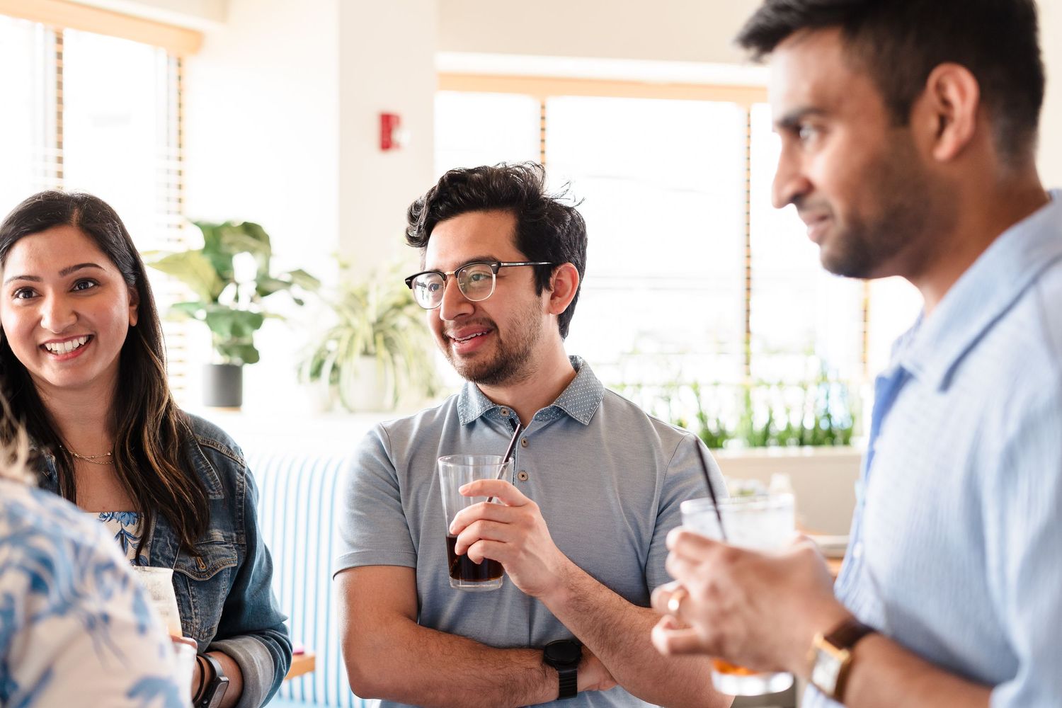 Coworkers socialize and smile while enjoying drinks together at a bright office gathering.
