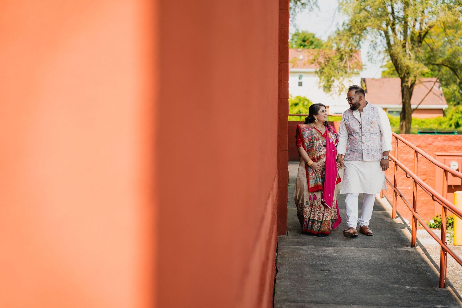 A couple in traditional Indian attire walking along an orange-walled corridor.
