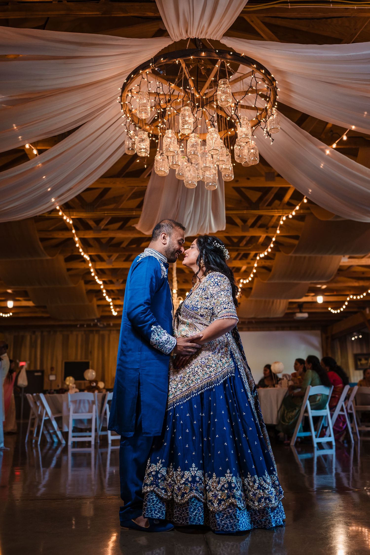Couple sharing a romantic moment under a crystal chandelier in an elegantly decorated reception hall.