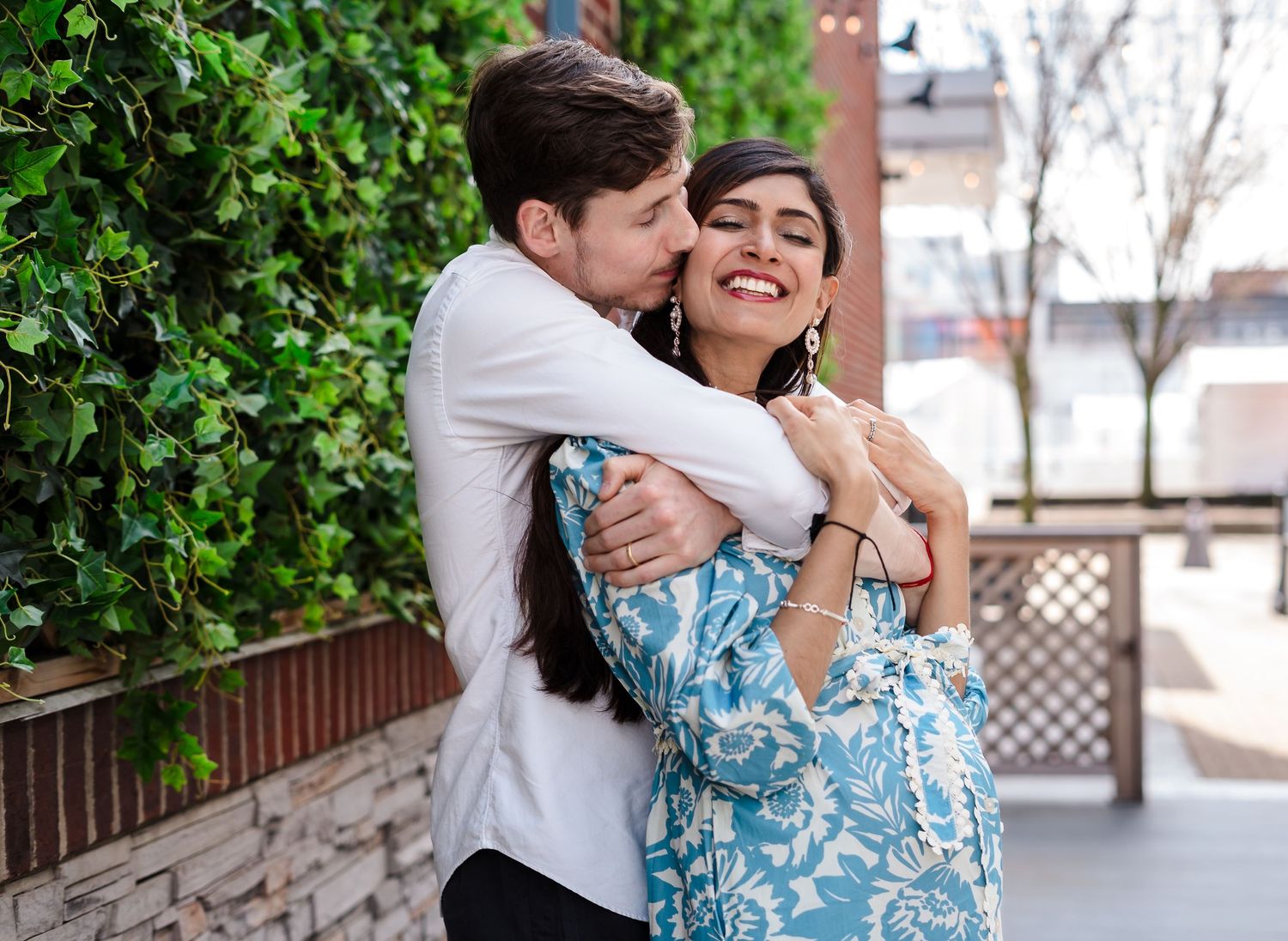 Couple sharing an affectionate moment outdoors by a leafy green wall.
