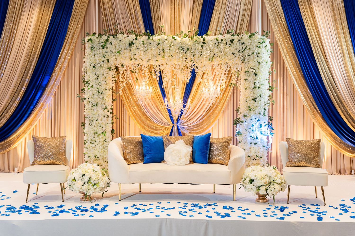 Elegant wedding stage with blue and ivory drapes, floral arch, and luxurious seating arrangement.