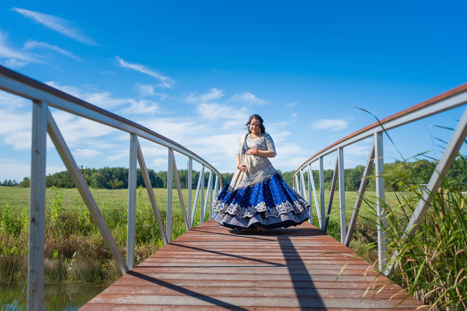 Flowing dress movement captured on wooden bridge against natural landscape and blue sky.