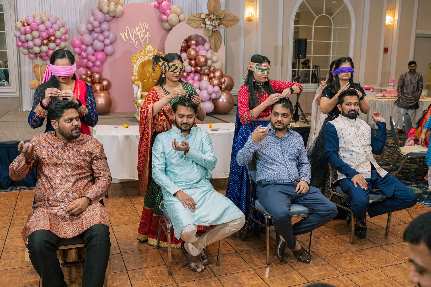 People seated in chairs at an indoor celebration with pink balloon decorations in the background.