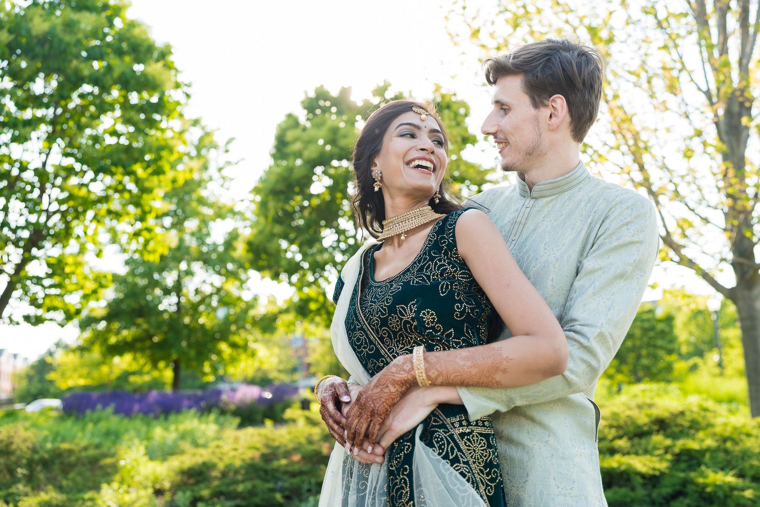 A couple laughs together outdoors during a summer engagement photoshoot.
