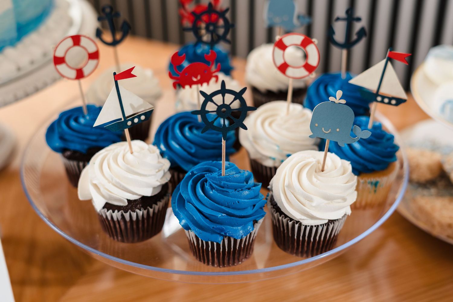 Nautical themed cupcakes decorated in blue and white frosting with miniature ship wheels and anchors.