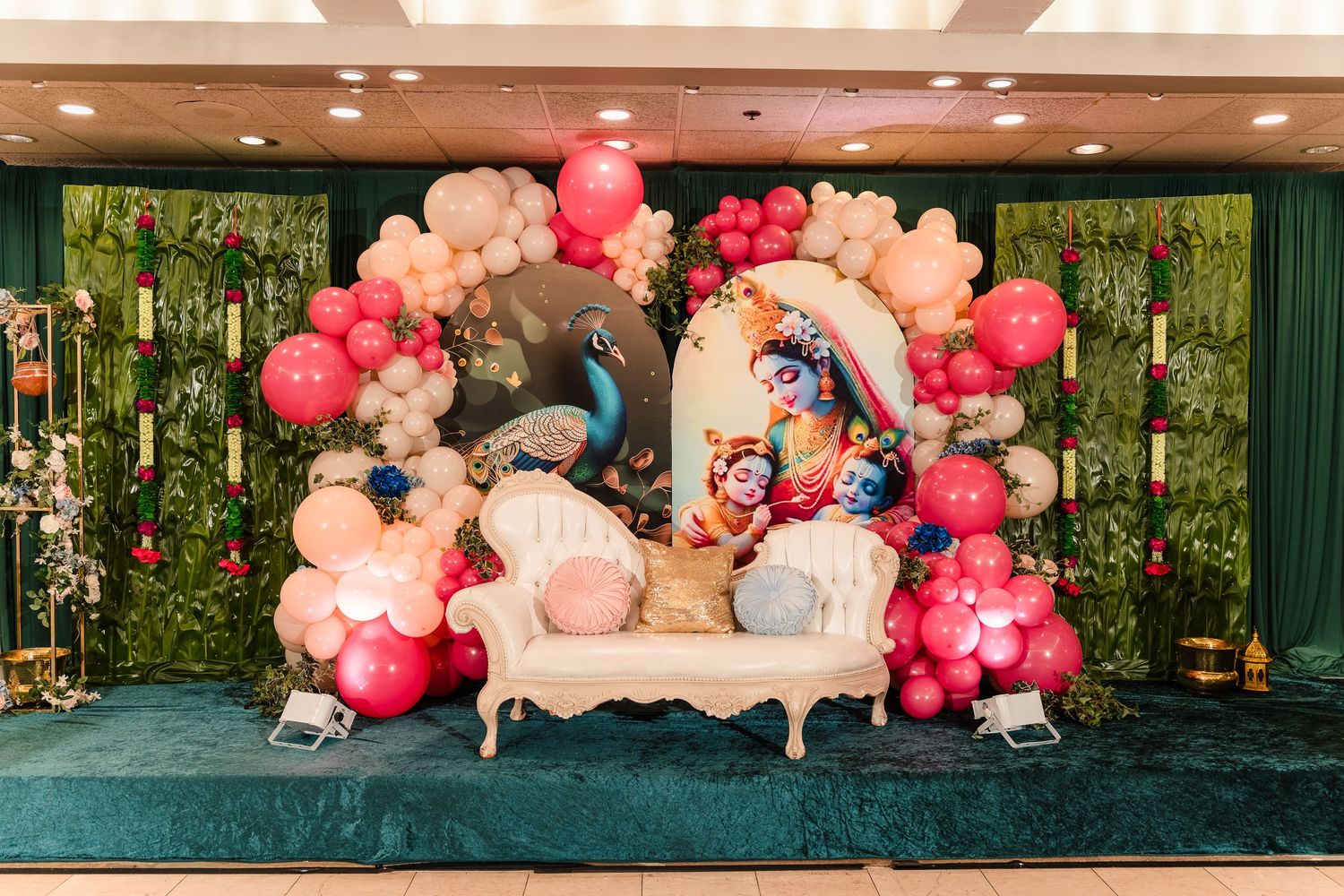 Luxurious party setup with pink balloon arch, vintage sofa, and elegant decorations against green backdrop.