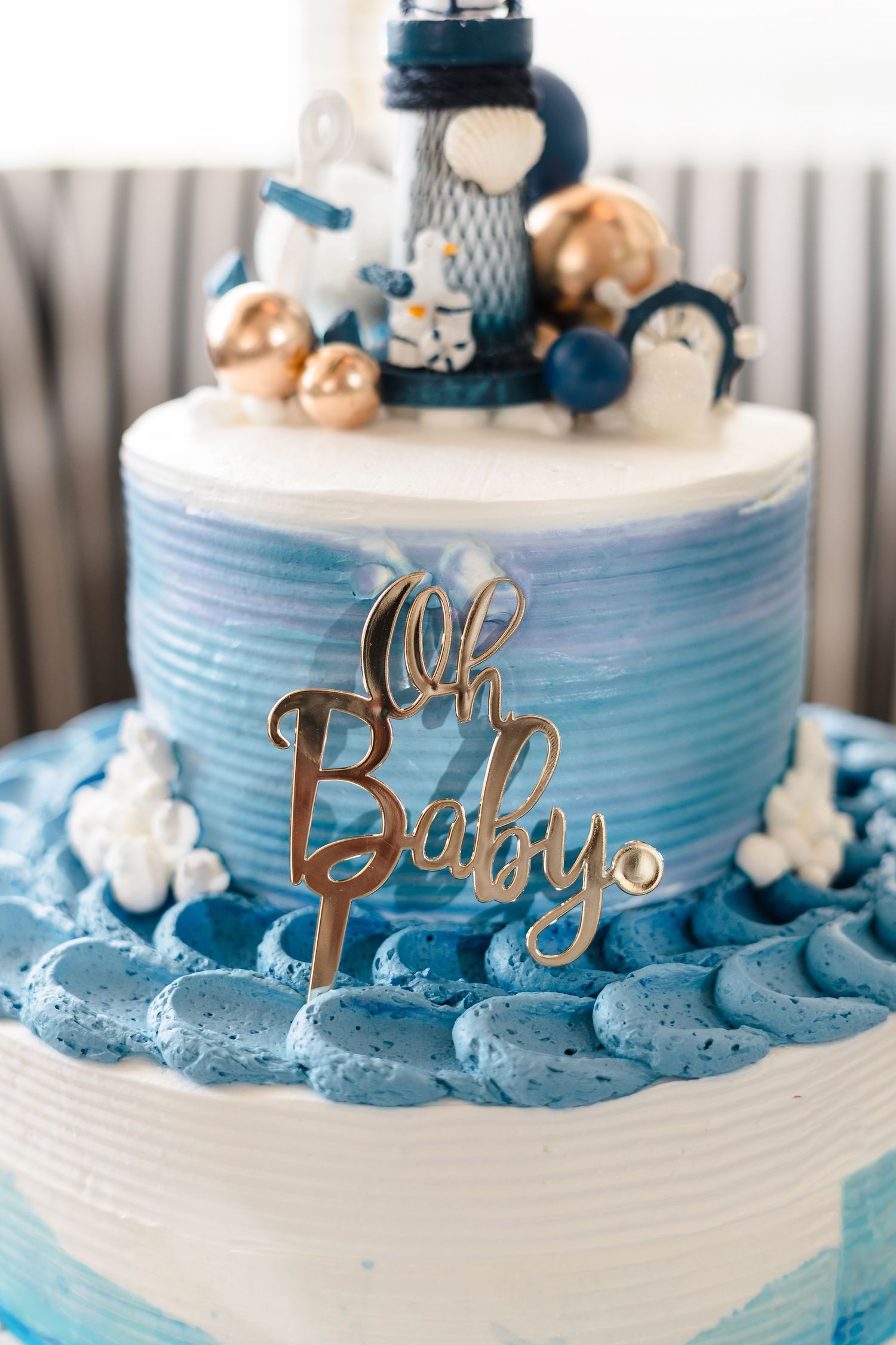 A blue and white baby shower cake decorated with macarons and a gold 'Oh Baby' topper on display.