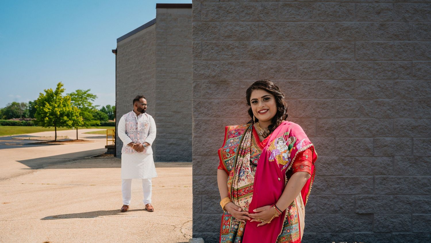 A creative engagement photo with traditional Indian attire against a modern building backdrop.