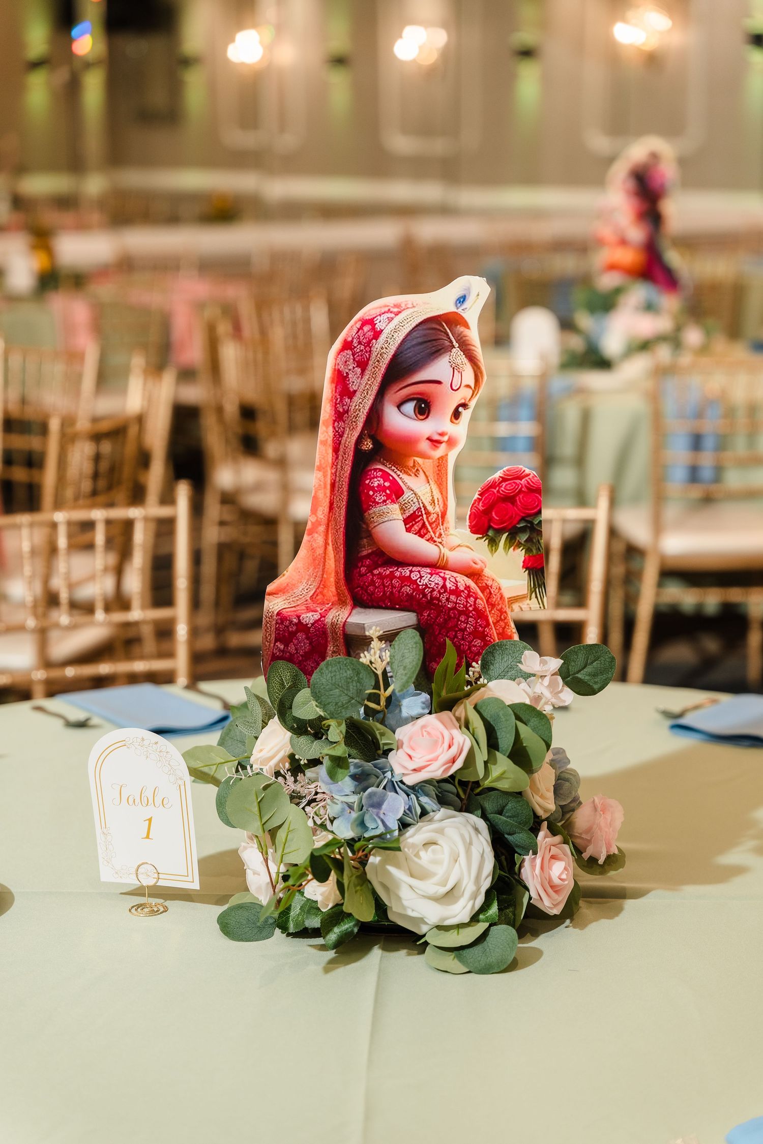 Decorative table centerpiece featuring a traditional Indian doll figure surrounded by pink and white roses.