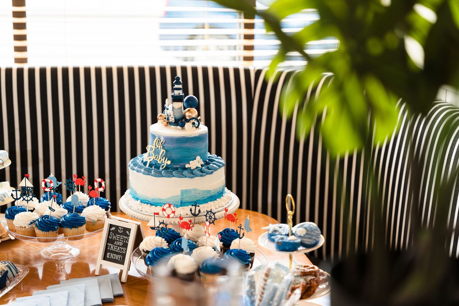 Blue and white wedding cake with ocean theme decorations and matching cupcakes displayed at a reception dessert table.