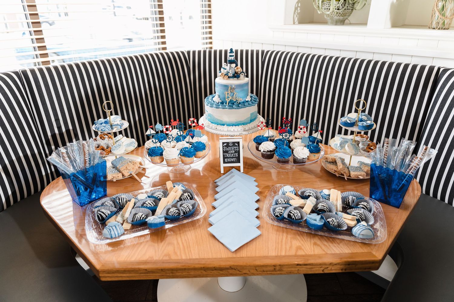 A dessert table with blue and white themed treats featuring a tiered cake, cupcakes, and snacks on a wooden surface.