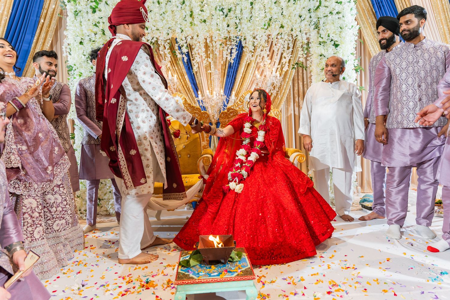 A joyous celebration with people at a traditional ceremony featuring red and gold decor with confetti on the floor.