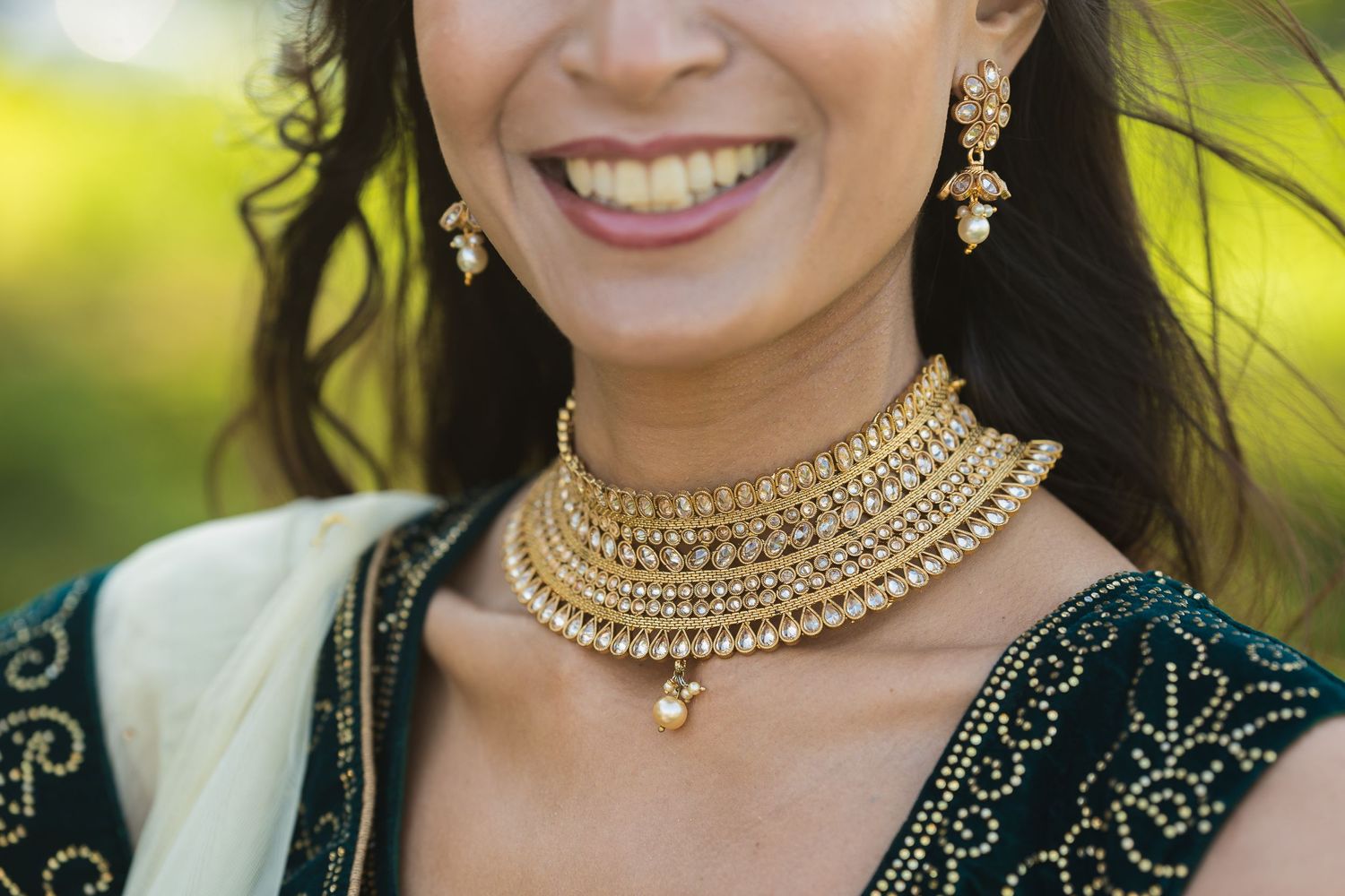 Close up of ornate gold choker necklace with pearls worn with emerald green embroidered traditional outfit.