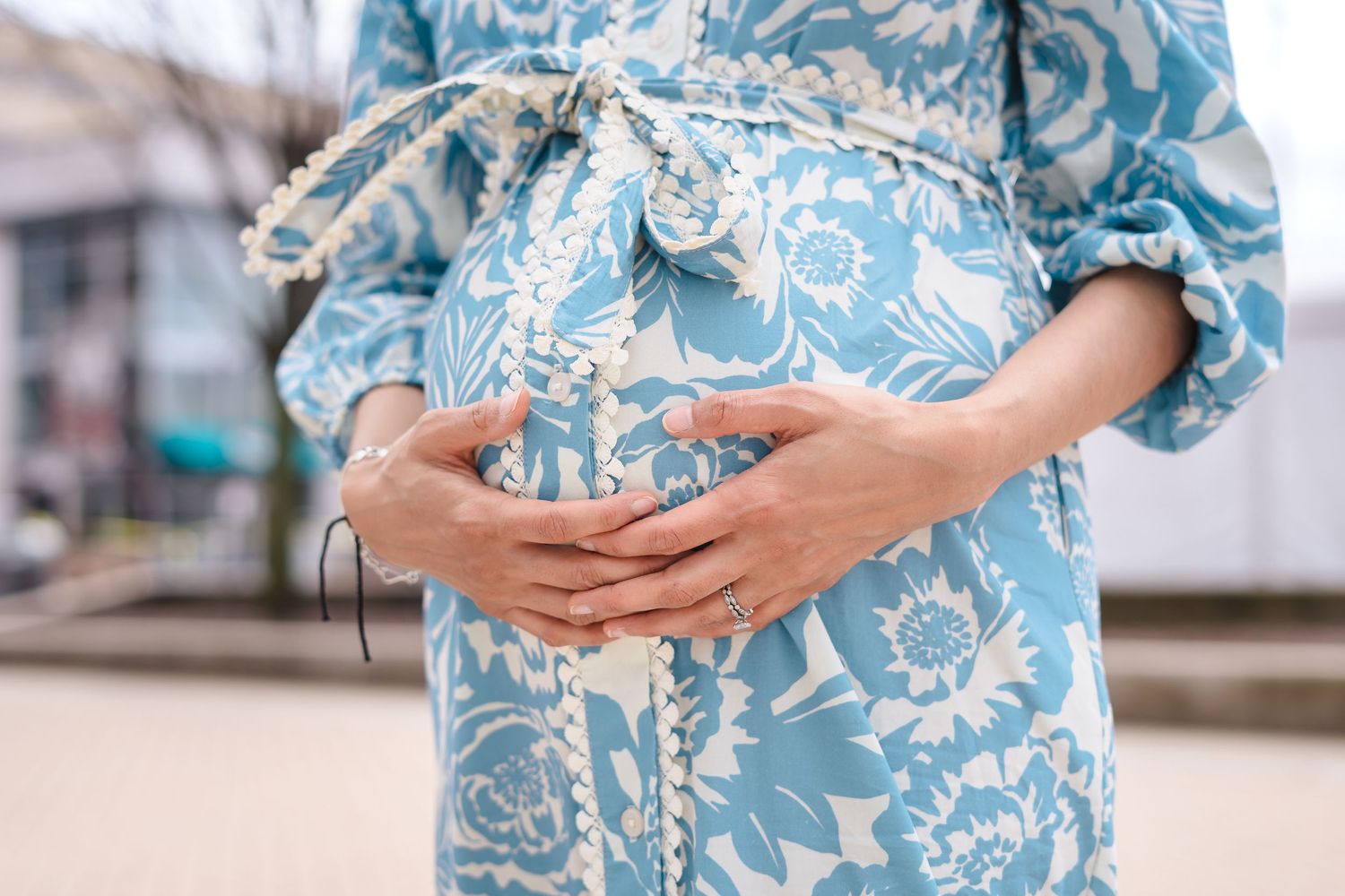 Close up of hands cradling a baby bump in a blue and white floral maternity dress.