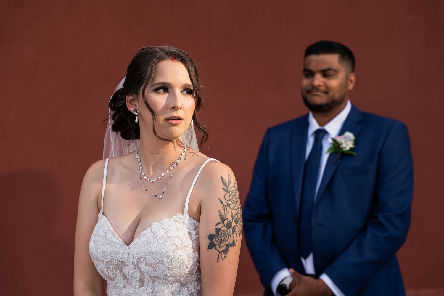 A couple shares a moment during their wedding ceremony against a terracotta colored wall.