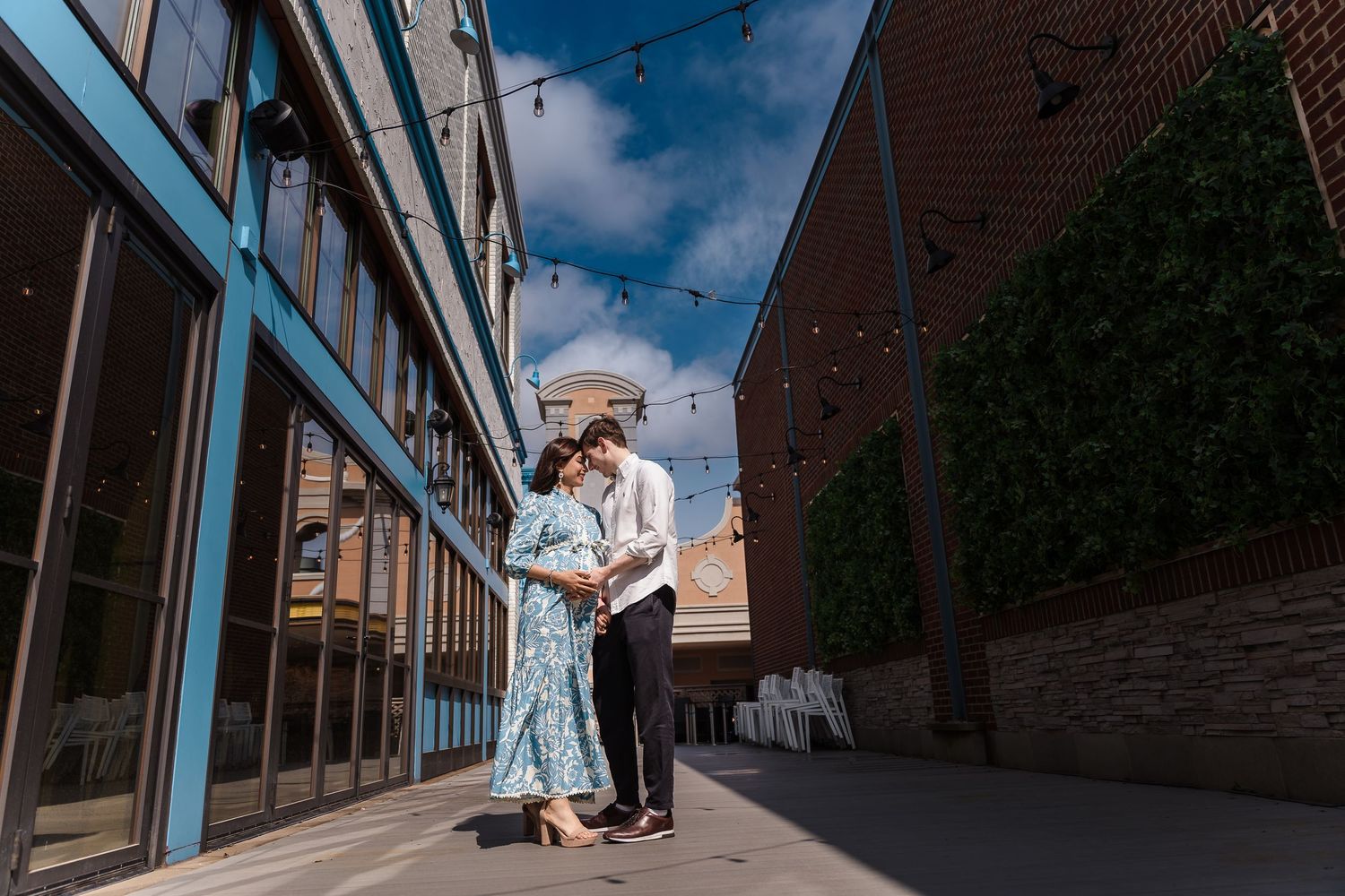 A couple embraces on a sunny day outside a brick building with blue storefront windows and climbing ivy walls.