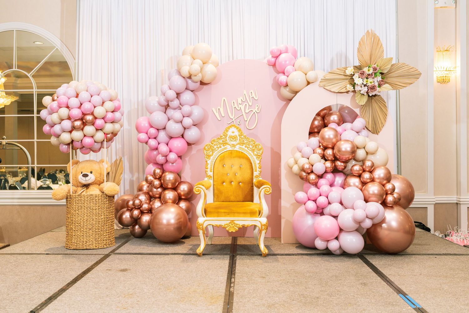 Luxurious event setup with ornate gold chair and balloon decorations in pink and copper tones.