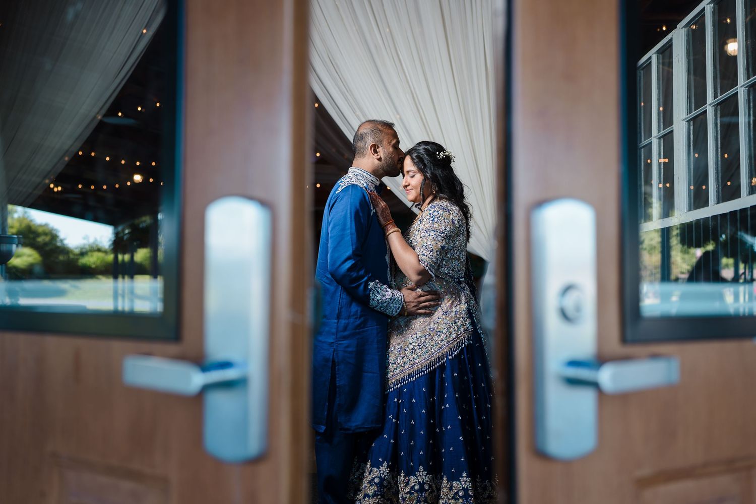 Couple posing between glass doors in formal attire with dramatic lighting.