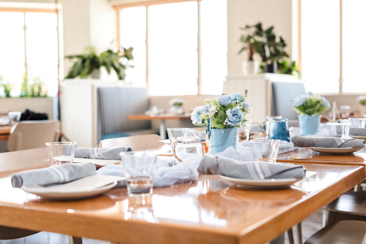 A modern restaurant table set with clean white plates and blue floral centerpieces in bright sunlit dining room.