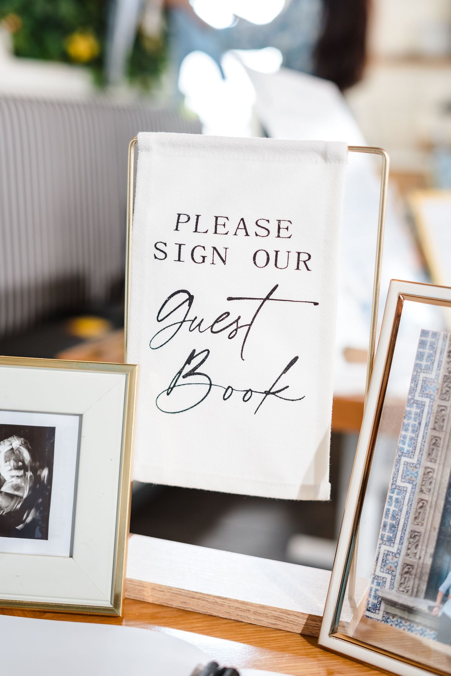 An elegant wedding guest book sign in black calligraphy displayed on a table with framed photos.