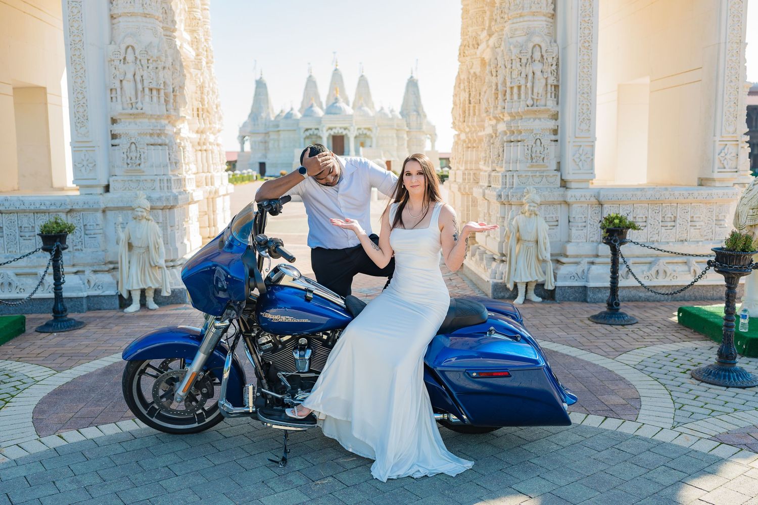 Wedding couple posing with blue motorcycle against elegant white architectural backdrop.
