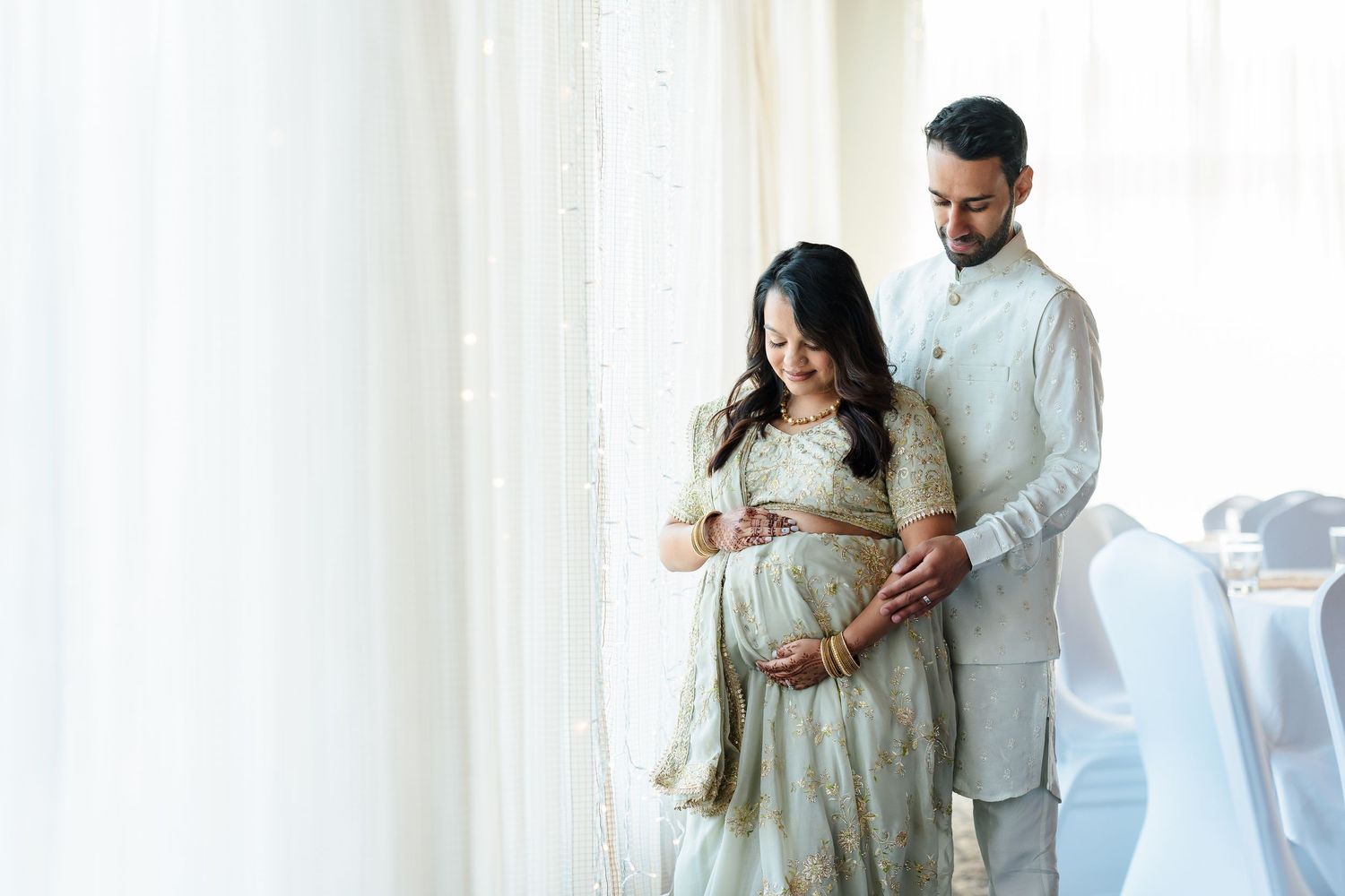Tender maternity moment captured by window light in elegant traditional attire.