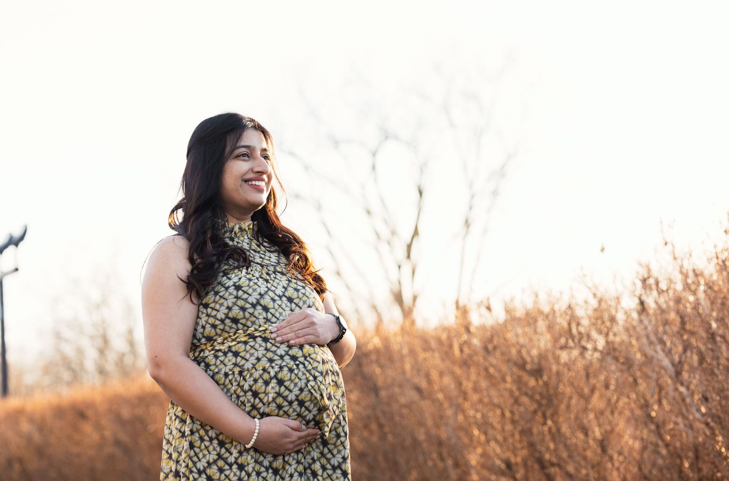 Joyful maternity portrait with expecting mother in patterned dress at golden hour.