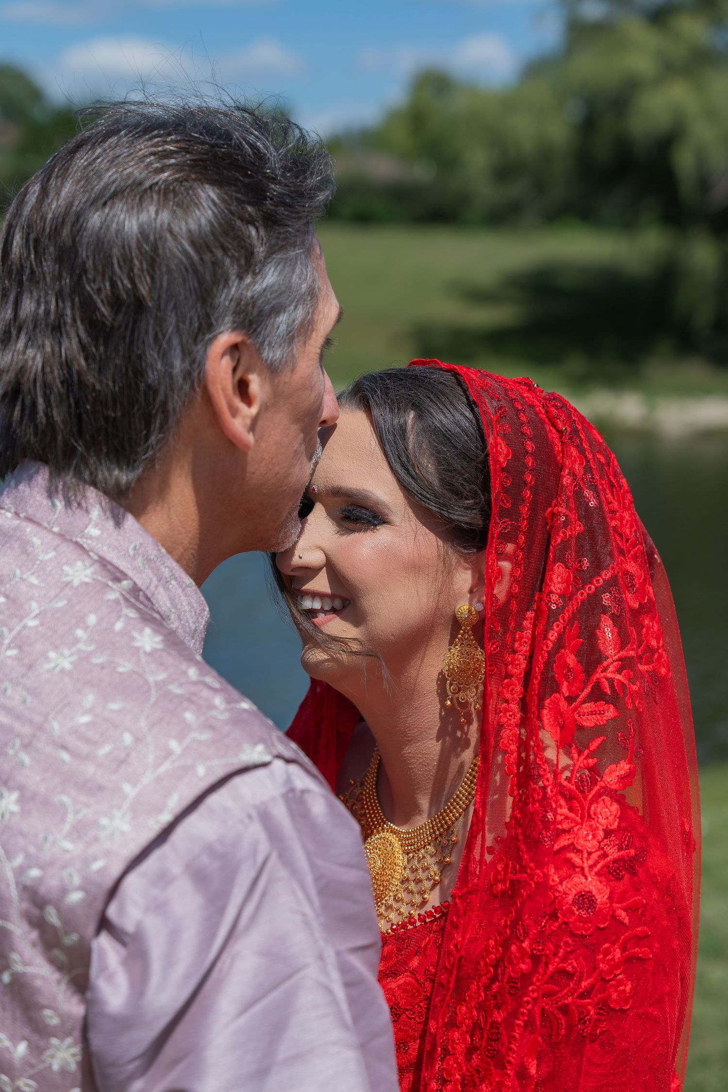 Intimate moment captured outdoors with red bridal veil and traditional wedding attire.